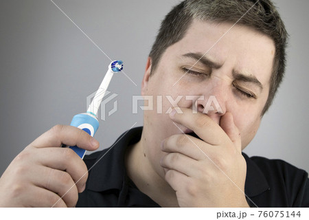 Sleepy man brushes his teeth with an electric brush. Oral hygiene concept. Tired man caring for teeth 76075144