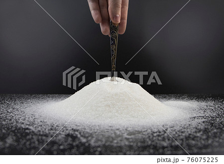 Spoon in sugar on a black background. The concept of addiction to sweets. Macro photo of granulated sugar. Spoon in sugar on a black background. The concept of addiction to sweets. Macro photo of granulated sugar. 76075225