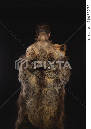 Low key portrait of a bearded war shaman in bearskin with an ancient ax in his hands. High quality cosplay of the ancient werewolf war. Back view Low key portrait of a bearded war shaman in bearskin with an ancient ax in his hands. High quality cosplay of the ancient werewolf war. Back view 76075275