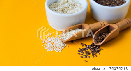 Wooden spoons with flax and sesame seeds lies in a white mortar on a yellow background. Healthy eating. Keto diet. Wooden spoons with flax and sesame seeds lies in a white mortar on a yellow background. Healthy eating. Keto diet. 76076218