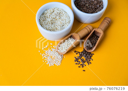 Wooden spoons with flax and sesame seeds lies in a white mortar on a yellow background. Healthy eating. Keto diet. 76076219