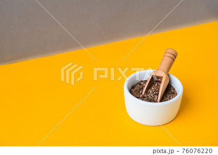 Wooden spoon with flax seeds lies in a white mortar on a yellow background. Healthy eating. Keto diet. Minimalistic concept in isometric style in trendy colors. Wooden spoon with flax seeds lies in a white mortar on a yellow background. Healthy eating. Keto diet. Minimalistic concept in isometric style in trendy colors. 76076220
