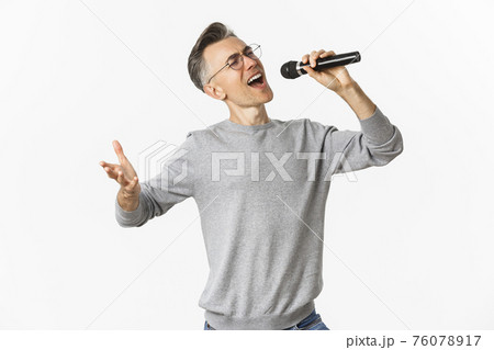 Portrait of passionate middle-aged man singing serenade in microphone, standing carefree over white background 76078917