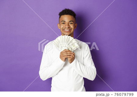 Portrait of handsome african-american man, showing money and smiling, got student loan, standing over purple background 76079799