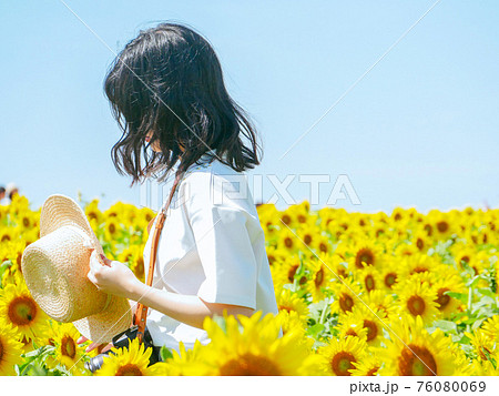 広大なひまわり畑で帽子を持っている白い服の女の子の写真素材