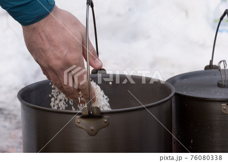 Close-up of a man's hand, which pours products into the pot. Cooking pot for cooking over a fire. Tourism 76080338