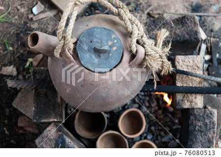 A steaming teapot and tea cups. Tea preparation in a clay pot on a fire. A camping trip, a journey. A steaming teapot and tea cups. Tea preparation in a clay pot on a fire. A camping trip, a journey. 76080513