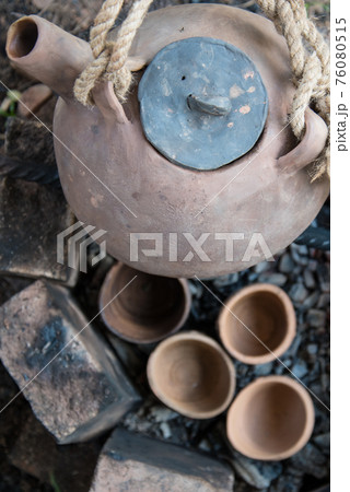 A steaming teapot and tea cups. Tea preparation in a clay pot on a fire. A camping trip, a journey. A steaming teapot and tea cups. Tea preparation in a clay pot on a fire. A camping trip, a journey. 76080515