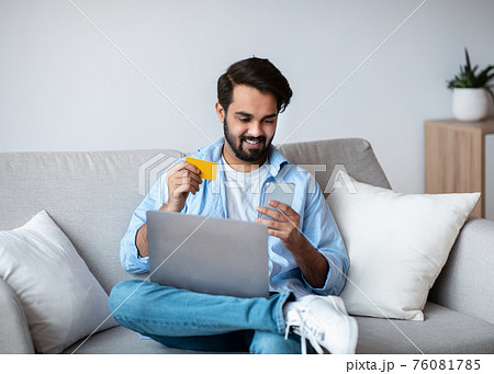 Eastern Man With Smartphone And Credit Card Making Online Payments At Home Eastern Man With Smartphone And Credit Card Making Online Payments At Home 76081785