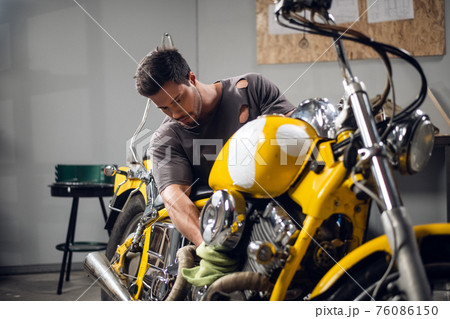 Private vehicle repair shop. Tuning a yellow chopper by a young mechanic. Private vehicle repair shop. Tuning a yellow chopper by a young mechanic. 76086150