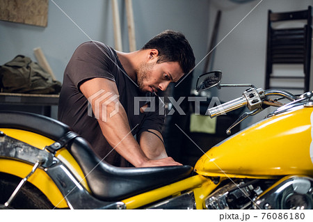 A modern young man in a t-shirt and jeans is engaged in bike diagnostics in a repair shop or garage. 76086180