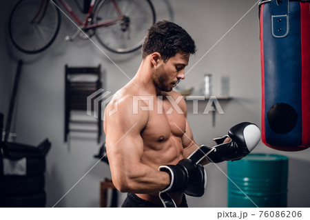 an experienced muscular athlete prepares for a fight, puts on Boxing gloves. 76086206