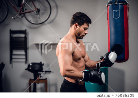 an experienced muscular athlete prepares for a fight, puts on Boxing gloves. 76086209