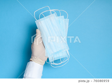 hands in medical gloves with a medical breathing mask on a blue background, health care prevention of coronavirus infection, as well as other viruses and pollution hands in medical gloves with a medical breathing mask on a blue background, health care prevention of coronavirus infection, as well as other viruses and pollution 76086959