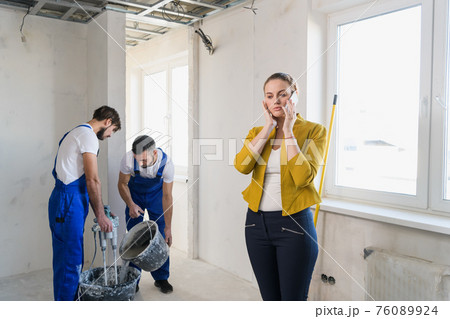 Female client uses phone in room with builders Female client uses phone in room with builders 76089924