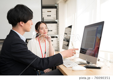 パソコンの画面を見ながら女性社員にアドバイスする上司 76090351