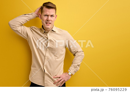 doubtful young caucasian guy stand thinking, scratch back of head 76095229