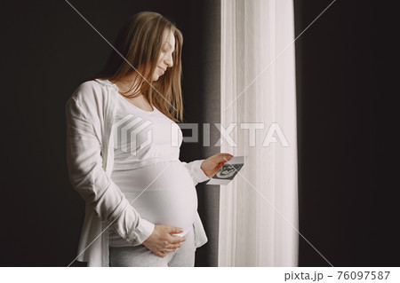 Pregnant woman stands by the window and looks at photo 76097587