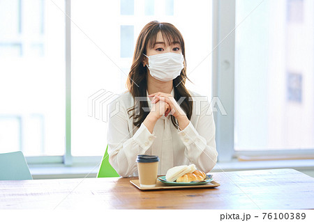 カフェでマスクをして食事をする若い女性 76100389