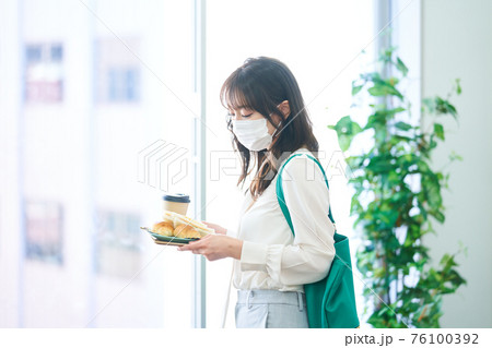 カフェでマスクをして食事をする若い女性 76100392