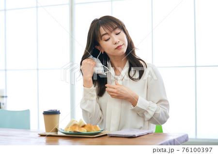 カフェでマスクをして食事をする若い女性 76100397