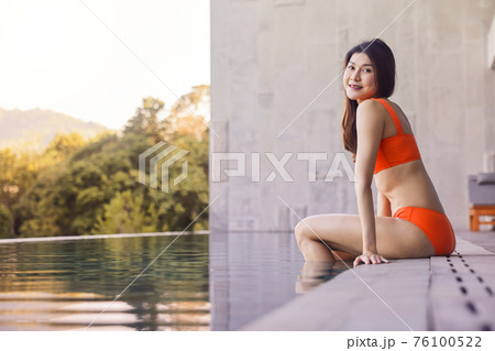 Portrait beautiful young asian woman smiling happy wear the orange bikini in relaxing sitting by swimming pool in hotel resort for leisure in vacation 76100522