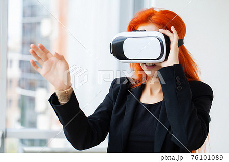 Young woman wearing virtual reality goggles in modern coworking studio. Young woman wearing virtual reality goggles in modern coworking studio. 76101089