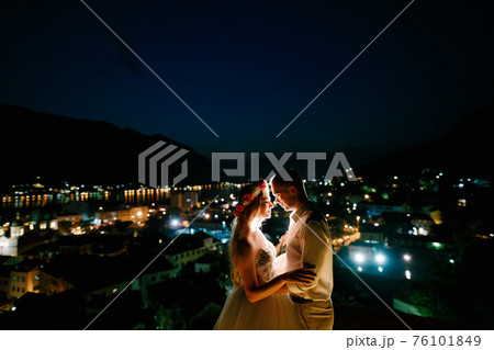 The bride and groom embrace at sunset on the observation deck above the old town of Kotor, close-up The bride and groom embrace at sunset on the observation deck above the old town of Kotor, close-up 76101849