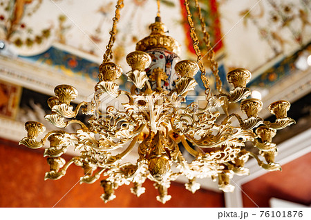 Close-up of an antique gold Italian chandelier. A chandelier-chandelier on gilded chains hangs against the background of the painted ceiling. 76101876