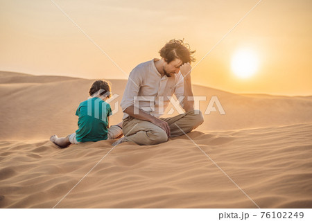 Relationship problems between father and son. Family conflict. Dad and son have a heated relationship, sit in the hot desert with their backs to each other and do not want to talk 76102249