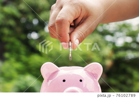 Close-up shot of a woman putting a coin in a piggy bank. Money saving concept. 76102789