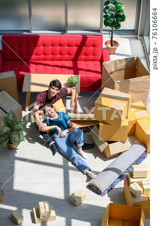 Top view of young couple smiling, relaxing and resting on the floor after unpacking cardboard boxes in new house with cardboard boxes on floor Top view of young couple smiling, relaxing and resting on the floor after unpacking cardboard boxes in new house with cardboard boxes on floor 76106664
