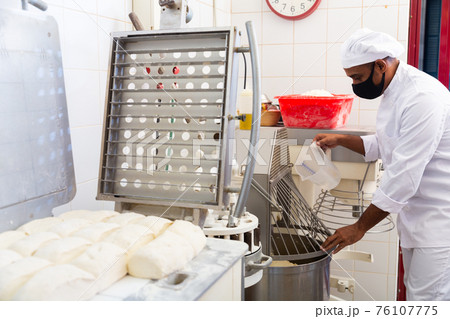 Baker controlling dough making in kneading machine in bakery 76107775