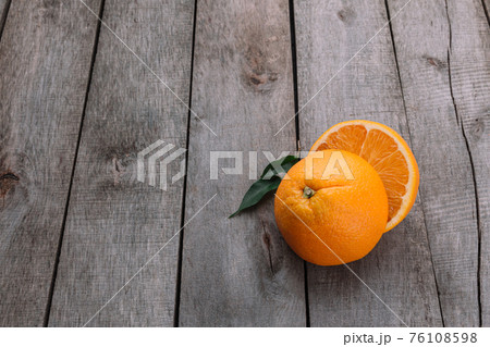 Halves of orange fruit on gray wooden background. Orange pulp and green leaves 76108598