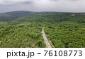 Aerial view from drone going through road on the mountain with green forest. View from the drone of the curve road. 76108773