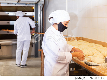 Woman baker dividing raw dough into portions in bakery 76109517