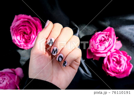 AMOR word on nails manicure hold Pink rose flower on black silk fabric. Minimal flat lay nature. Female hand. Love AMOR word on nails manicure hold Pink rose flower on black silk fabric. Minimal flat lay nature. Female hand. Love 76110191