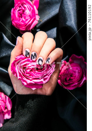 AMOR word on nails manicure hold Pink rose flower on black silk fabric. Minimal flat lay nature. Female hand. Love 76110192