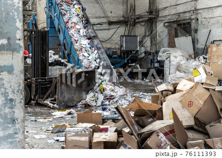 Shreding wastepaper mill conveyor belt for recycling paper wrap, garbage and cardboard against bales of used carton boxes collected for recycle and reuse at industrial plant or factory.Sustainable 76111393