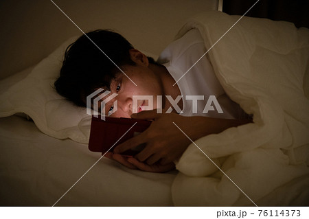 布団でスマホを見る若い男性・夜更かしする男性イメージ 76114373