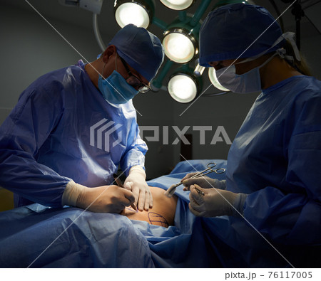 Surgeon and assistant doing plastic surgery in operating room. 76117005