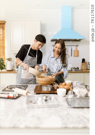Asian couple Help each other to make a bakery In a romantic atmosphere in the kitchen at home. Young people work together to mix the ingredients in a wooden bowl before stirring them together. Asian couple Help each other to make a bakery In a romantic atmosphere in the kitchen at home. Young people work together to mix the ingredients in a wooden bowl before stirring them together. 76117610