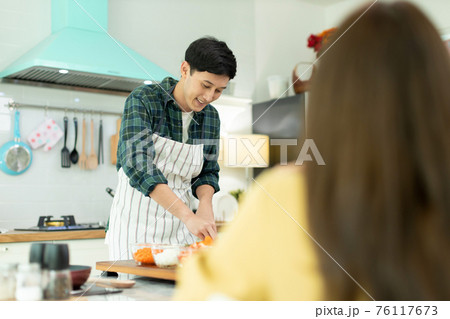 Husband slicing vegetables to prepare breakfast. With a young wife supporting him In a romantic atmosphere 76117673