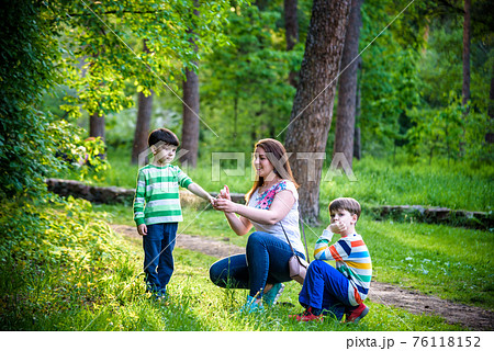 Young woman mother applying insect repellent to her two son before forest hike beautiful summer day or evening. Protecting children from biting insects at summer. Active leisure with kids 76118152
