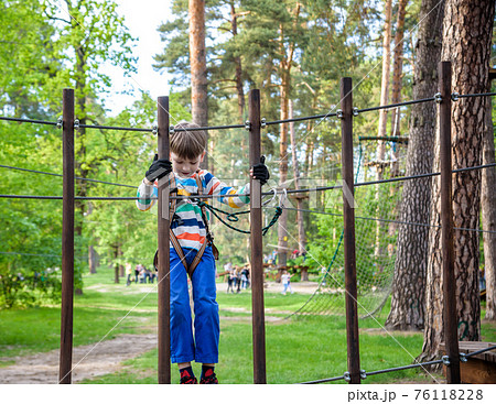 Cute boy enjoying a sunny day in a climbing adventure activity park. shadows from a rope Cute boy enjoying a sunny day in a climbing adventure activity park. shadows from a rope 76118228