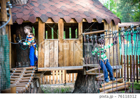 Two little boys playing together and having fun. Lifestyle family moment of siblings on playground. Kids friends play on tree house climbing on rope or stairs Two little boys playing together and having fun. Lifestyle family moment of siblings on playground. Kids friends play on tree house climbing on rope or stairs 76118312