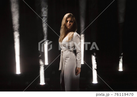 luxurious blonde plus size with white long hair posing in a long white dress on a dark stage luxurious blonde plus size with white long hair posing in a long white dress on a dark stage 76119470