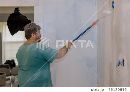 Rear view of painter paints the wall with a roller 76120656