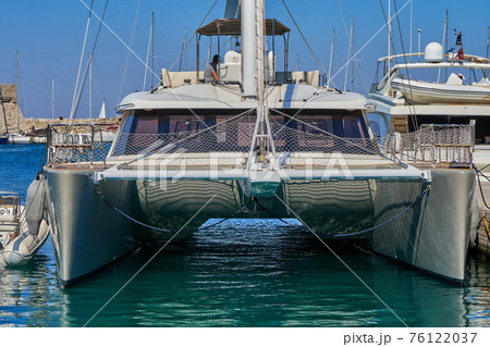 White shiny catamaran boat of modern design moored to pier on sea White shiny catamaran boat of modern design moored to pier on sea 76122037