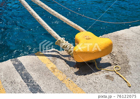 Yellow mooring bollard with rope on grey concrete pier Yellow mooring bollard with rope on grey concrete pier 76122075